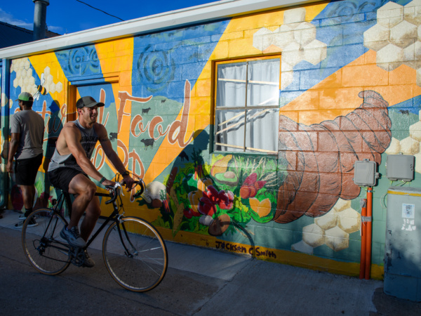 A man rides a bike in front of a mural.