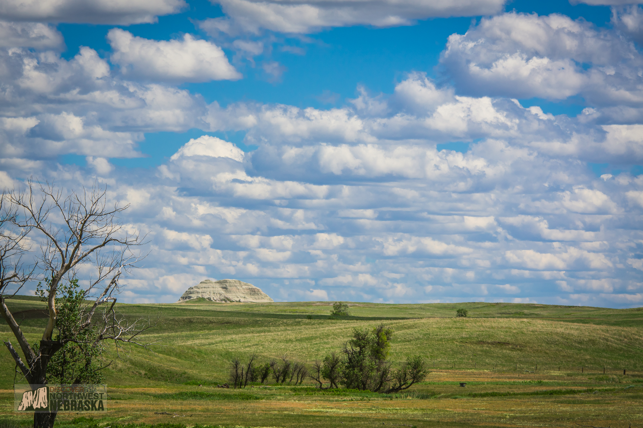 Butte protruding out of prairie with cloudy sky