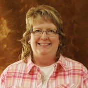 Head shot of a woman with shoulder length light brown hair and glasses in a pink plaid shirt.