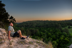 Man on cliff looking out at Nebraska National Forest trees