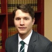 Head shot of a man in a suit and tie in front of a book case filled with books.