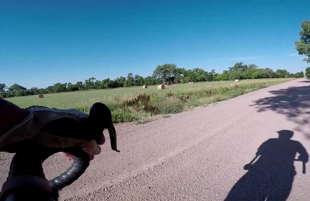 A gravel road stretches out in front of a set of bike handlebars and the shadow of the rider can be seen on the road.
