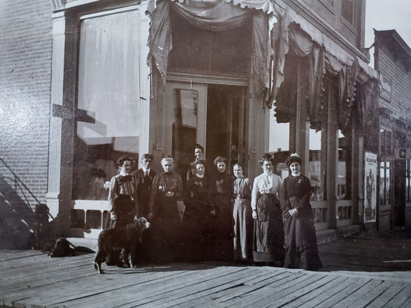 A historic black and white photo depicting several individuals standing in front of a building.