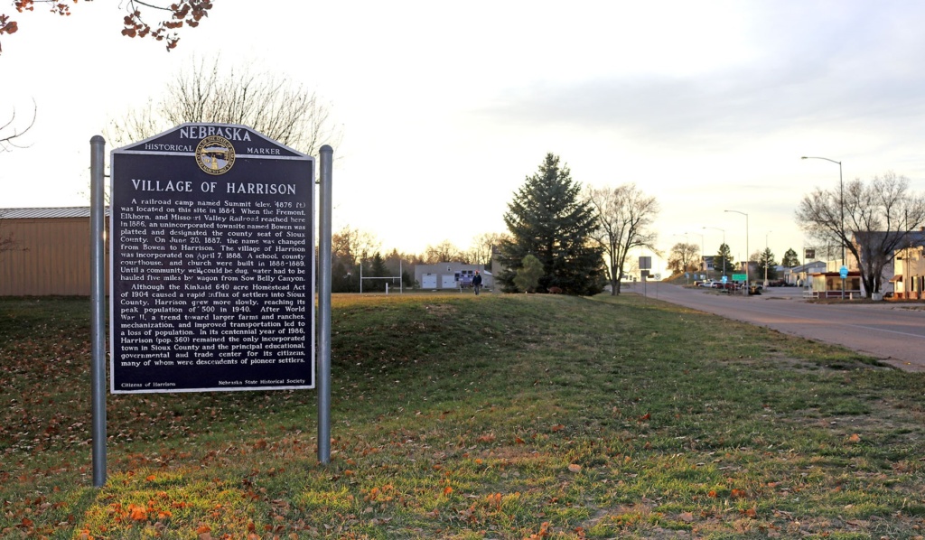 A blue state historical marker sits on green grass next to a highway.
