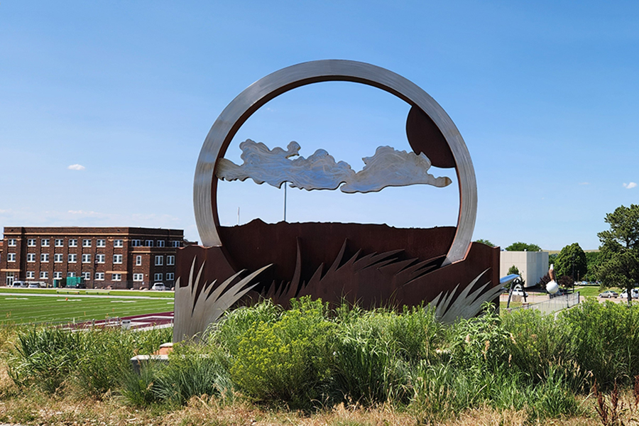 Sculpture with clouds and grass surrounded by vegetation on the Chadron State College Campus