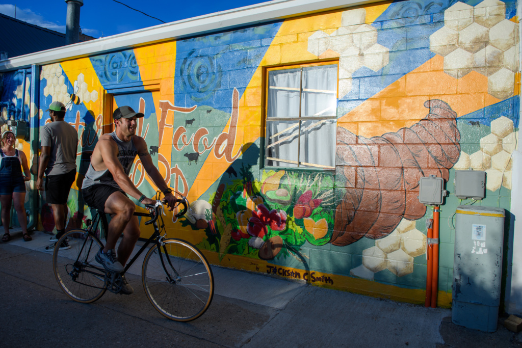 A man rides a bike in front of a mural.