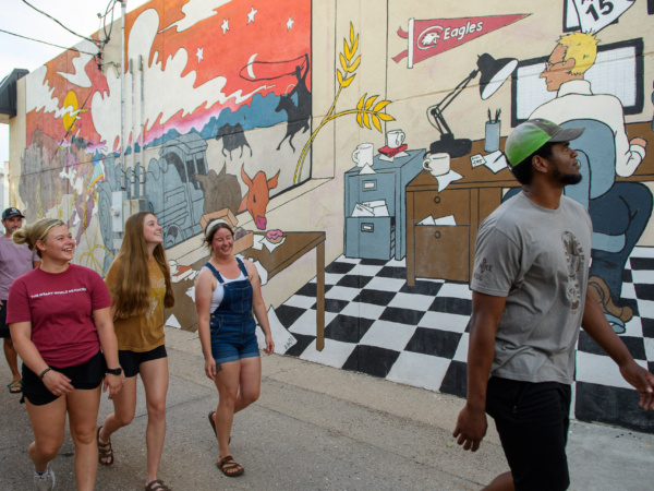 A group of people walking in front of a mural in Chadron's Art Alley.