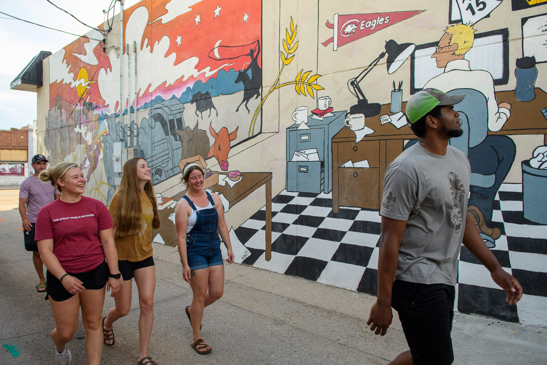A group of people walking in front of a mural in Chadron's Art Alley.