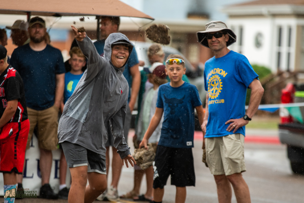 An individual throws a buffalo chip while others look on and cheer.