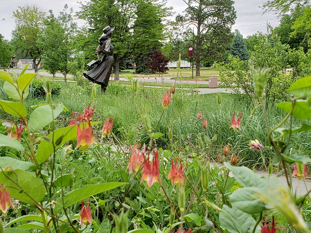 A statue of Mari Sandoz surrounded by red flowers