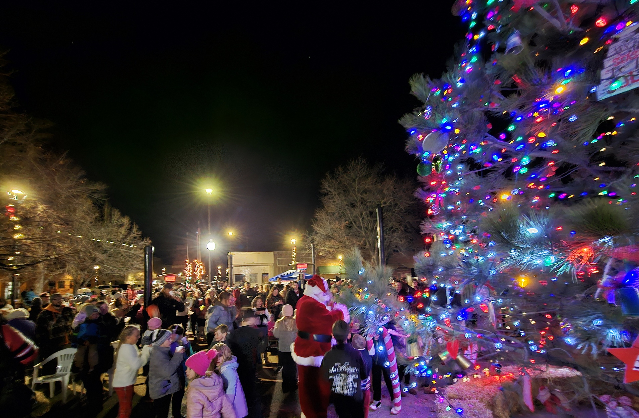 A crowd of people surround Santa and a Christmas tree