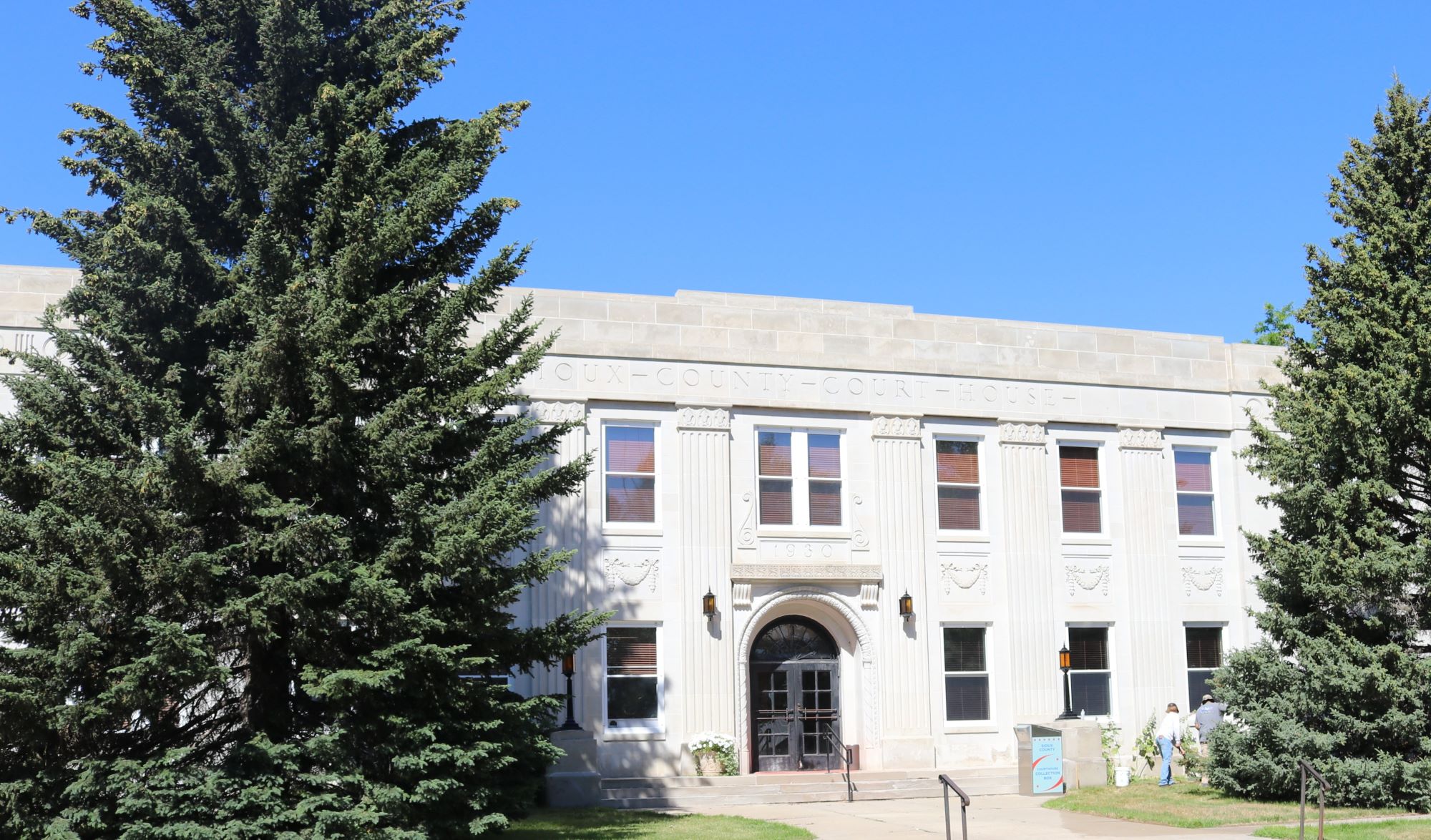A two story stone building flanked by trees.