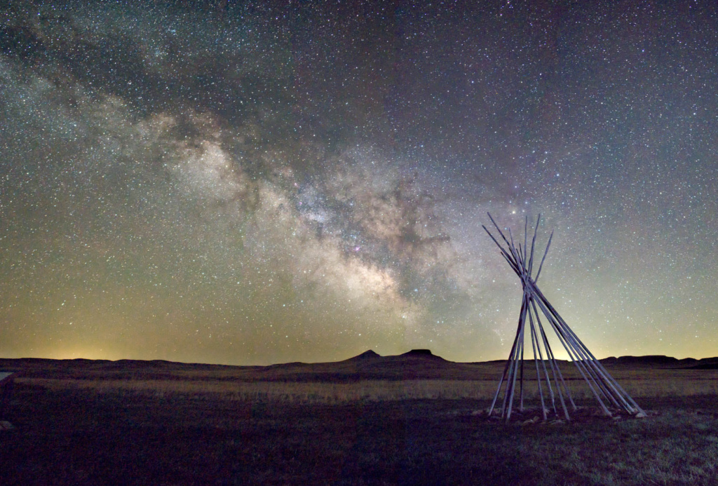 A tipi frame sits in relief against the Milky Way