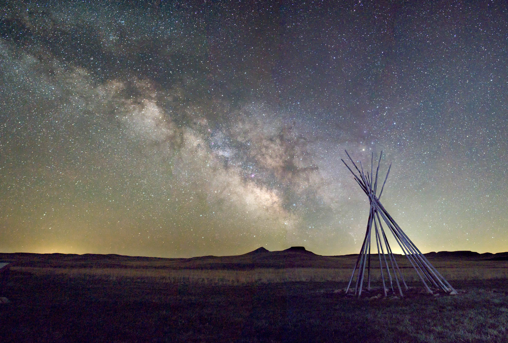 A tipi frame sits in relief against the Milky Way
