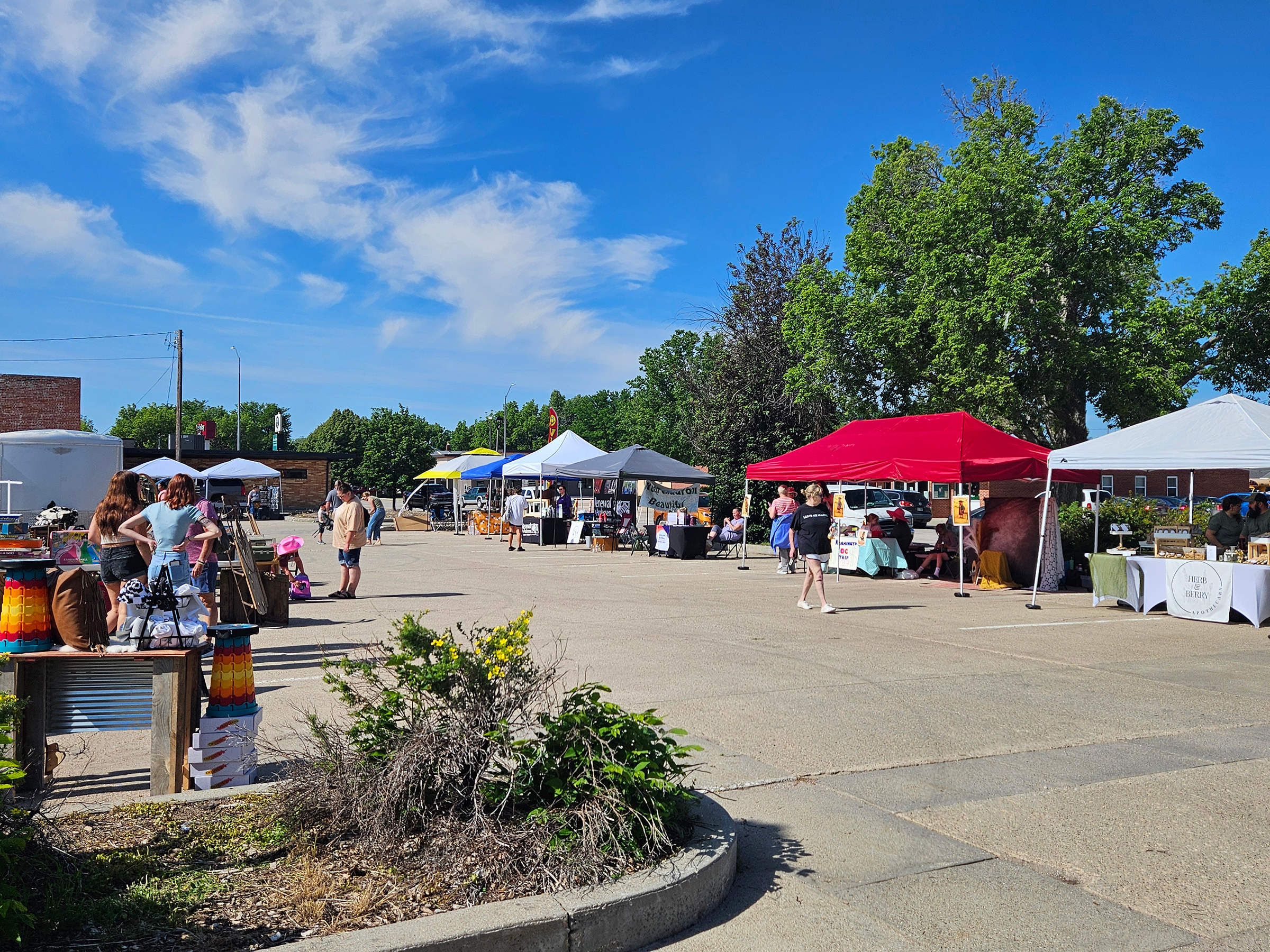 People shop at an outdoor craft and artisan market in a parking lot full of vendors under canopies.