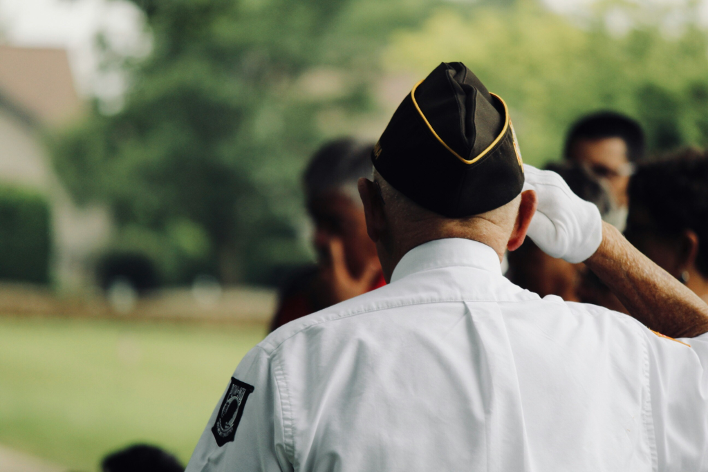 A uniformed retired veteran stands at attention with his back to the camera.