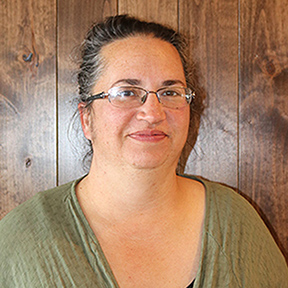 Head shot of a woman with her hair pulled up in a bun wearing glasses and a green shirt.